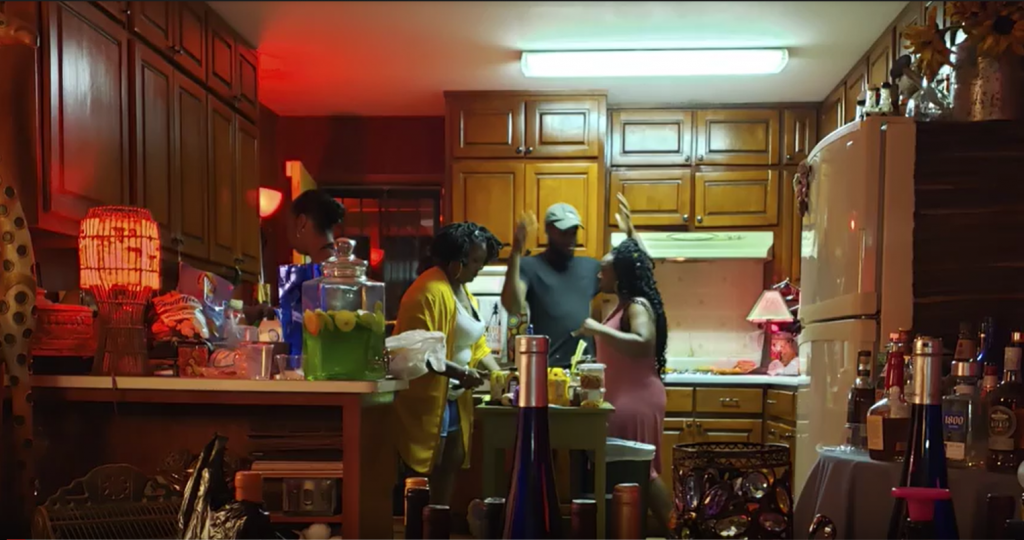 Two black women and a black man in a kitchen at a house party.